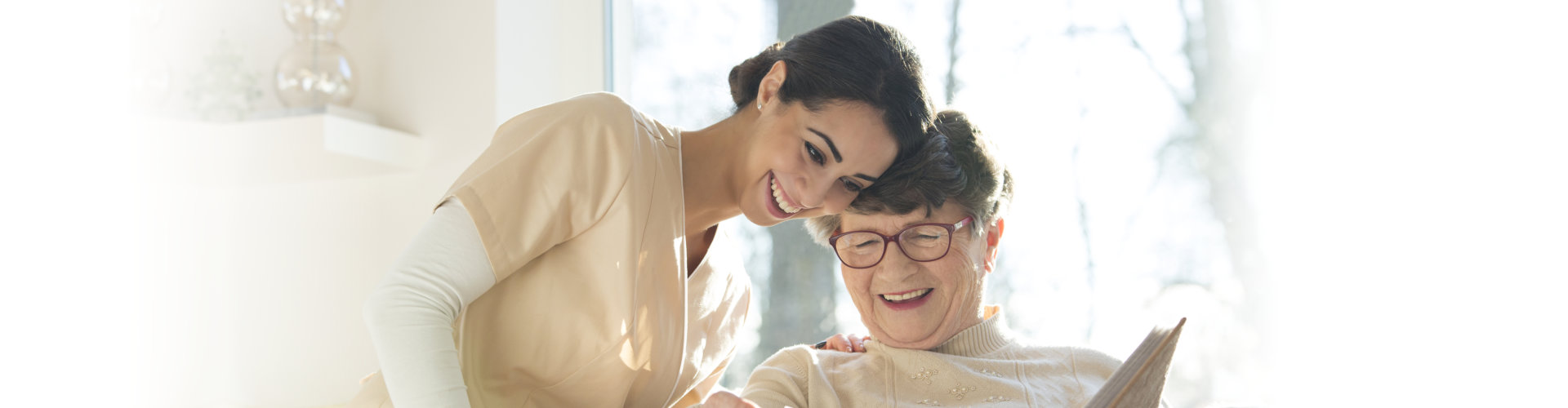 Smiling senior women watching photo album with happy caregiver